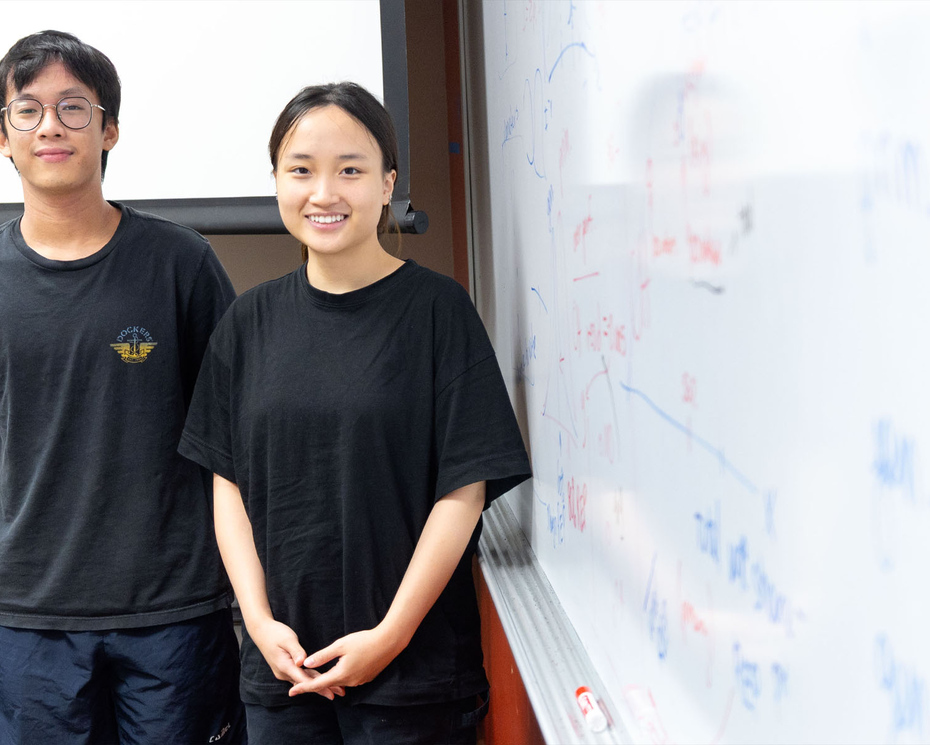 Photo of two Denison students Huy Phan and Linh Bui stand next to a dry-erase board filled with observations and notes.