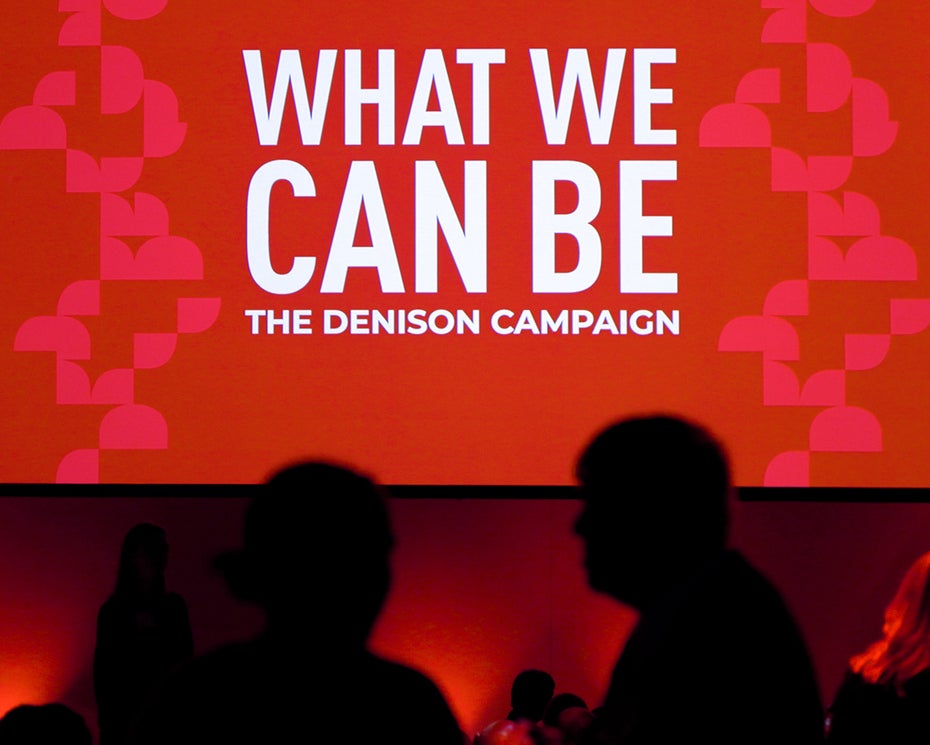 People mingle in front of a sign that says "What We Can Be."