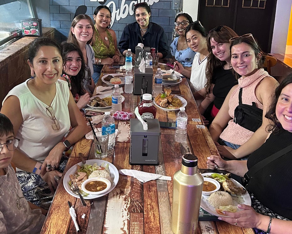 Nearly a dozen people sitting around a long wooden table filled with plates of food at a casual restaurant.