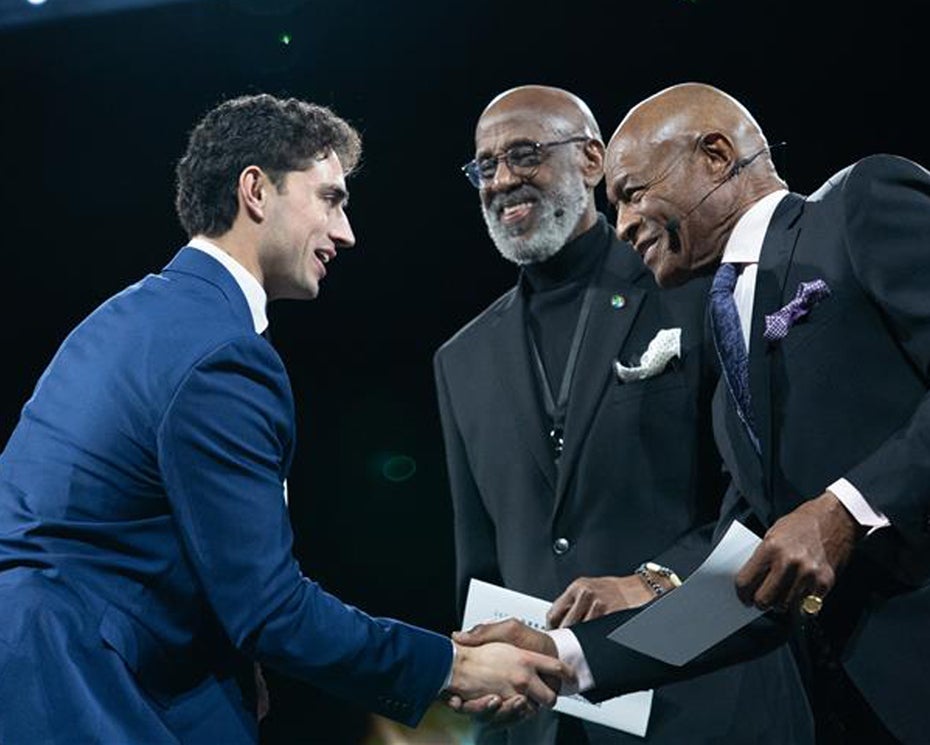 A man in a blue suit shakes hands with two men in suits as they hand him an award.