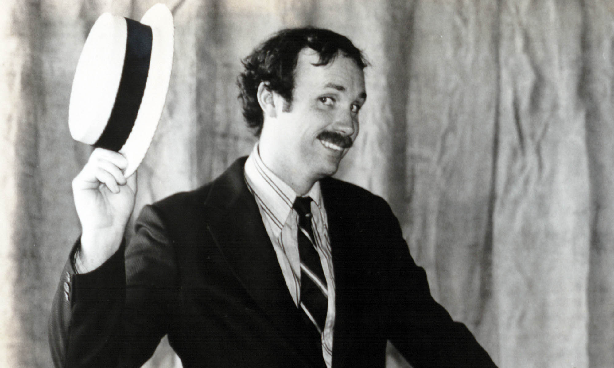Photo of a young Gary McAvay in a suit and tie, holding a classic straw boater hat.