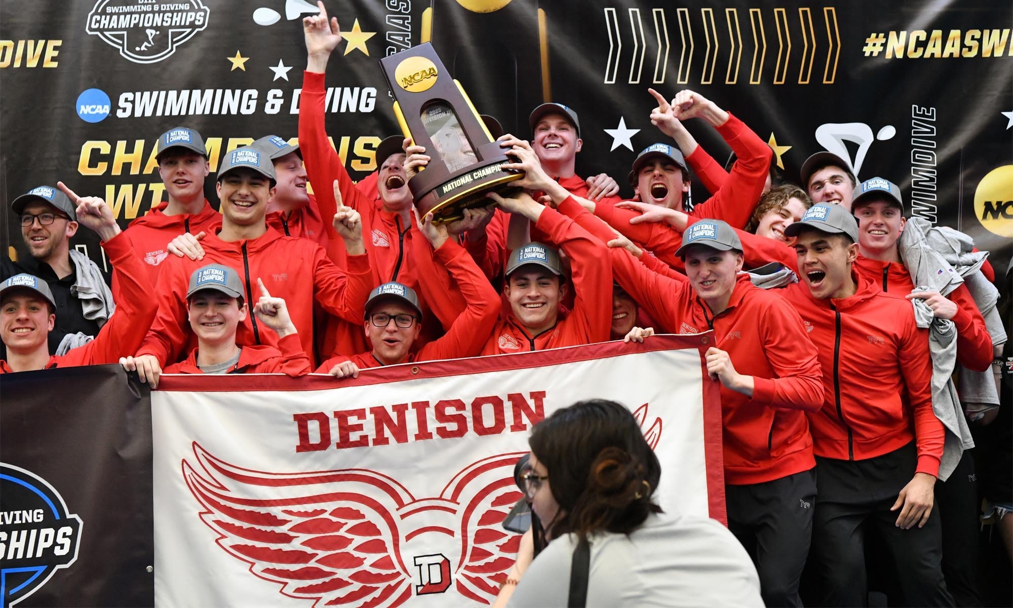 Denison men's swimming and diving team celebrates championship holding NCAA trophy.