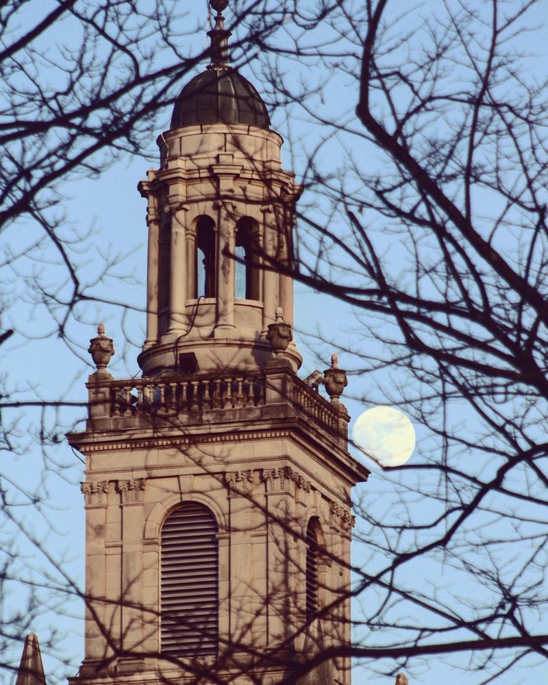 The top of Swasey Chapel seen through bare trees with the Moon rising in the background