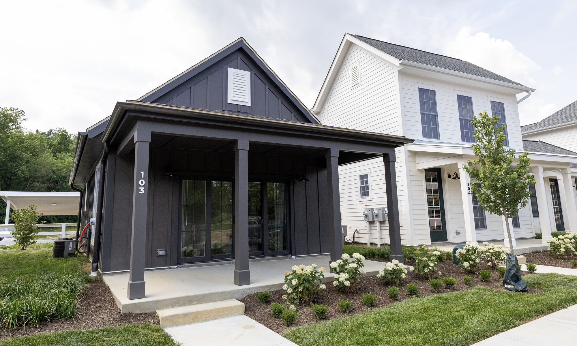 A one-story dark charcoal painted house next to a white two-story home viewed from the sidewalk.