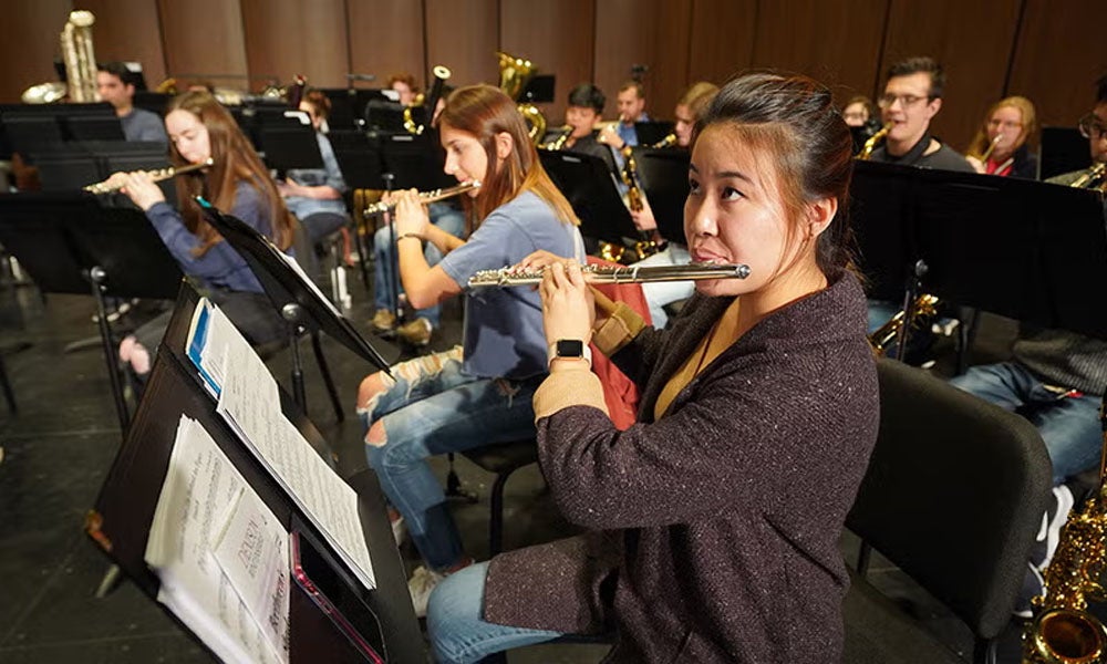 Close up of a student playing the flute on stage with an orchestra.