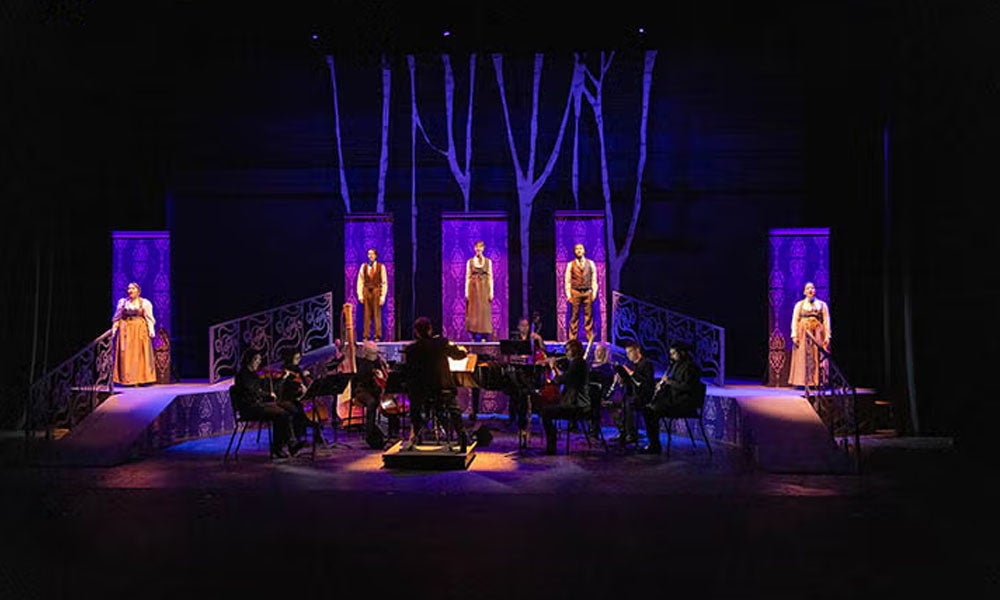 Production photo of a play with actors standing in dramatic lighting.