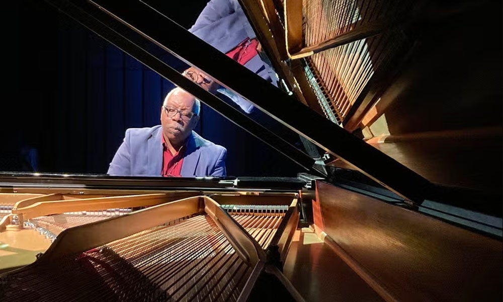 A photo of a pianist playing as seen through the open lid of a baby grand piano.