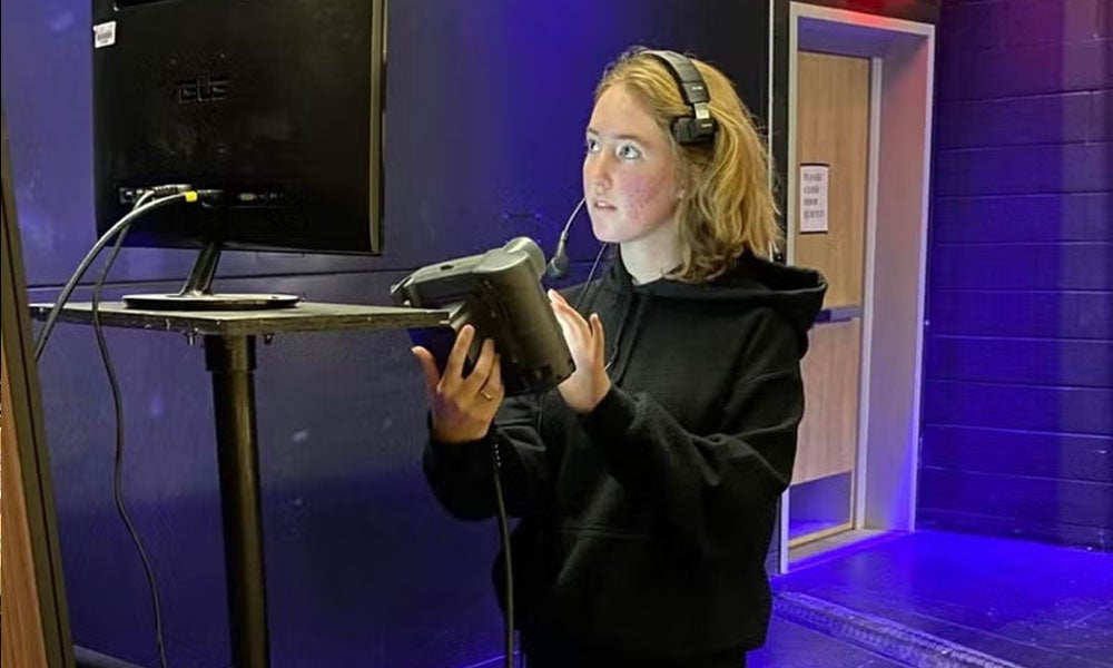 A women with headphones stands in the wings of a stage calling the show.