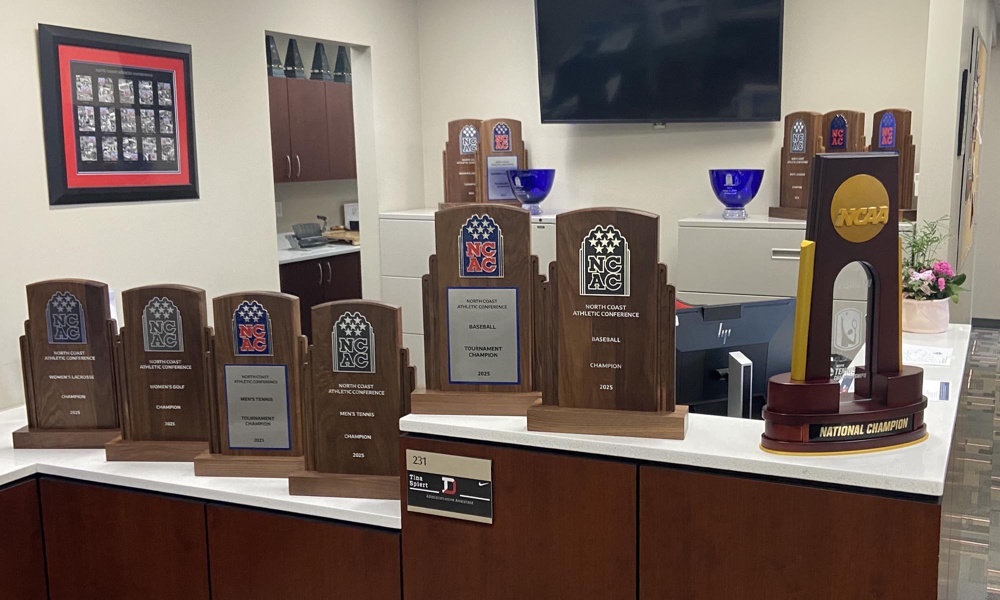 Multiple trophies from the 2024-25 season cover a large reception desk in the Athletic department's offices.