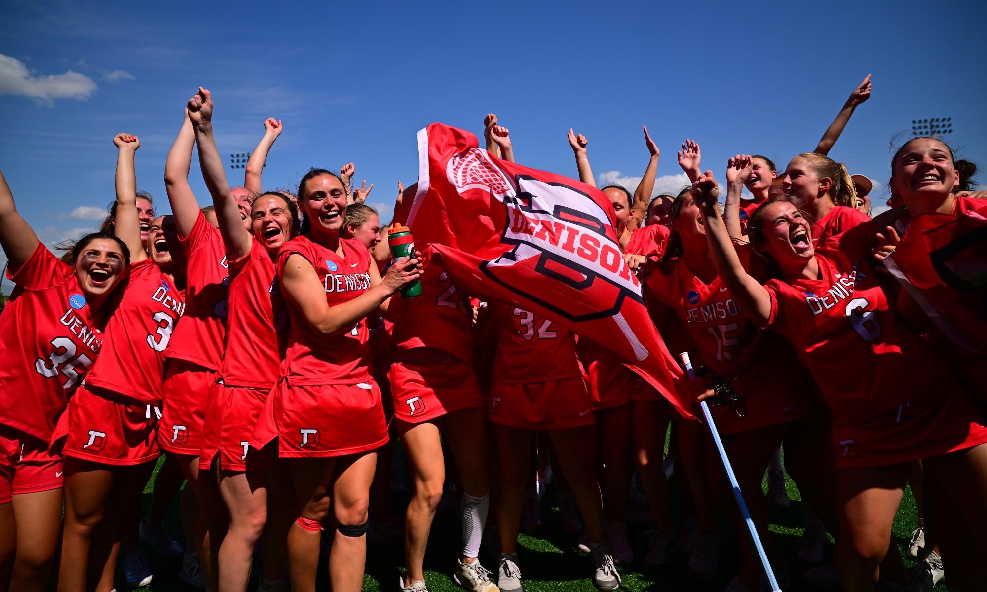 The Women's Lacross team cheers while waving a Denison flag.