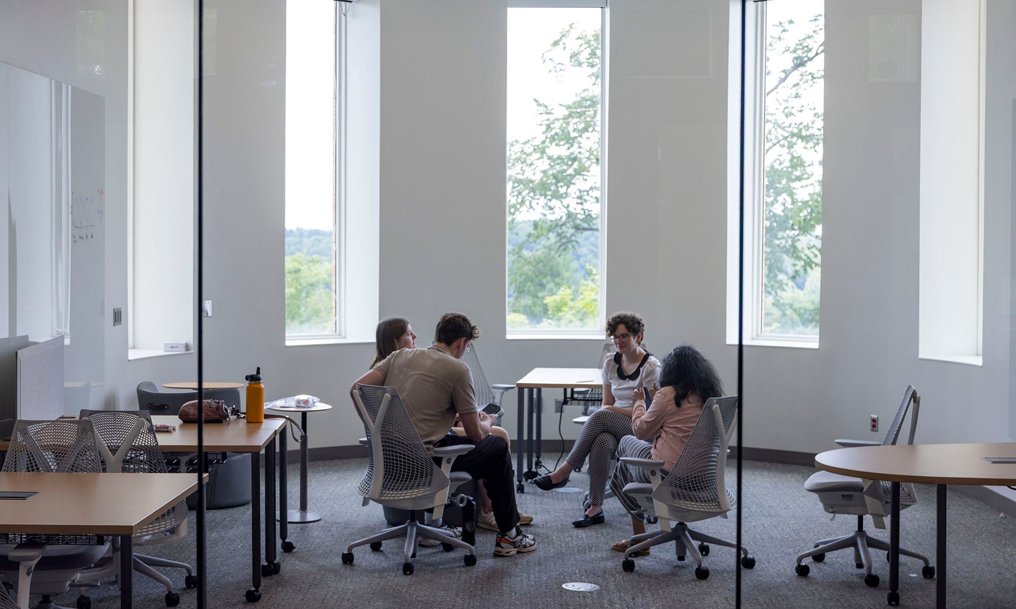 Four people sit in a small group discussion in a modern office room with large windows and natural light.