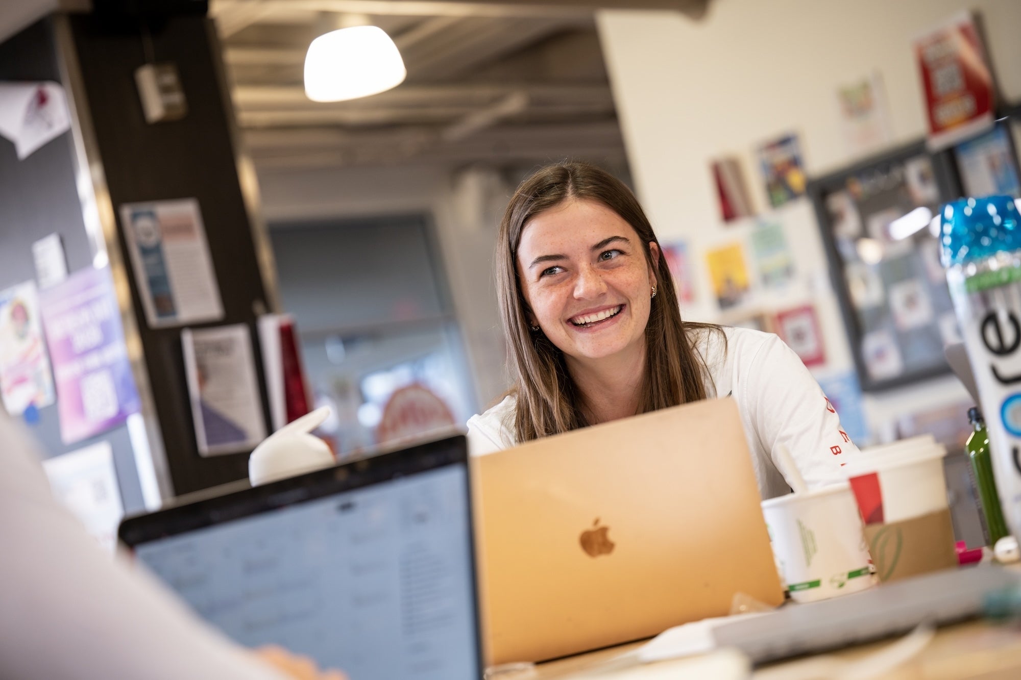 Student smiles at her friends as she works on her laptop