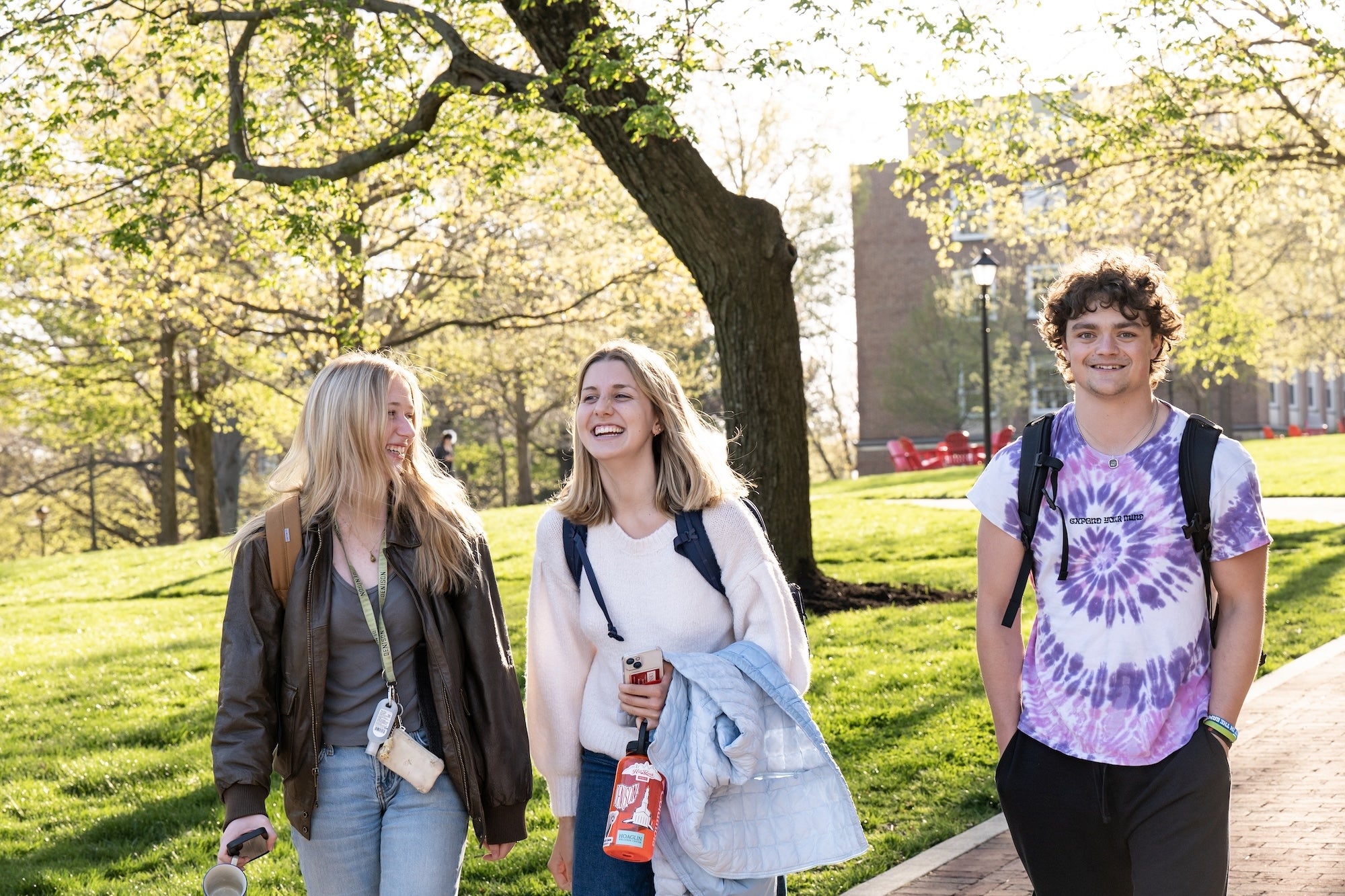 Three students chat as they walk across campus on a sunny day