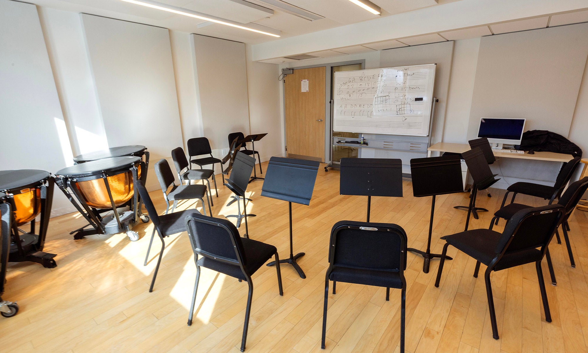 A brightly lit music room with chairs and music stands for up to a dozen people arranged in a circle.