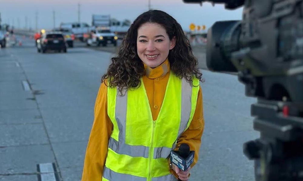 Lena Folke ’22 on a road with a microphone and neon-yellow vest in front of a news camera.