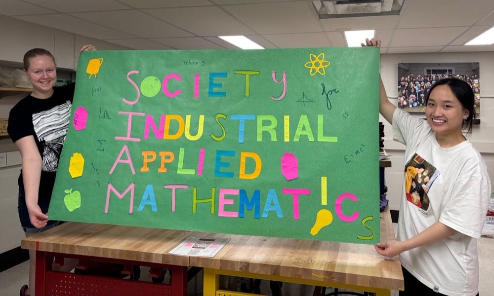 Two Denison students hold up a colorful banner that reads "Society for Industrial Applied Mathematics" and features math symbols.