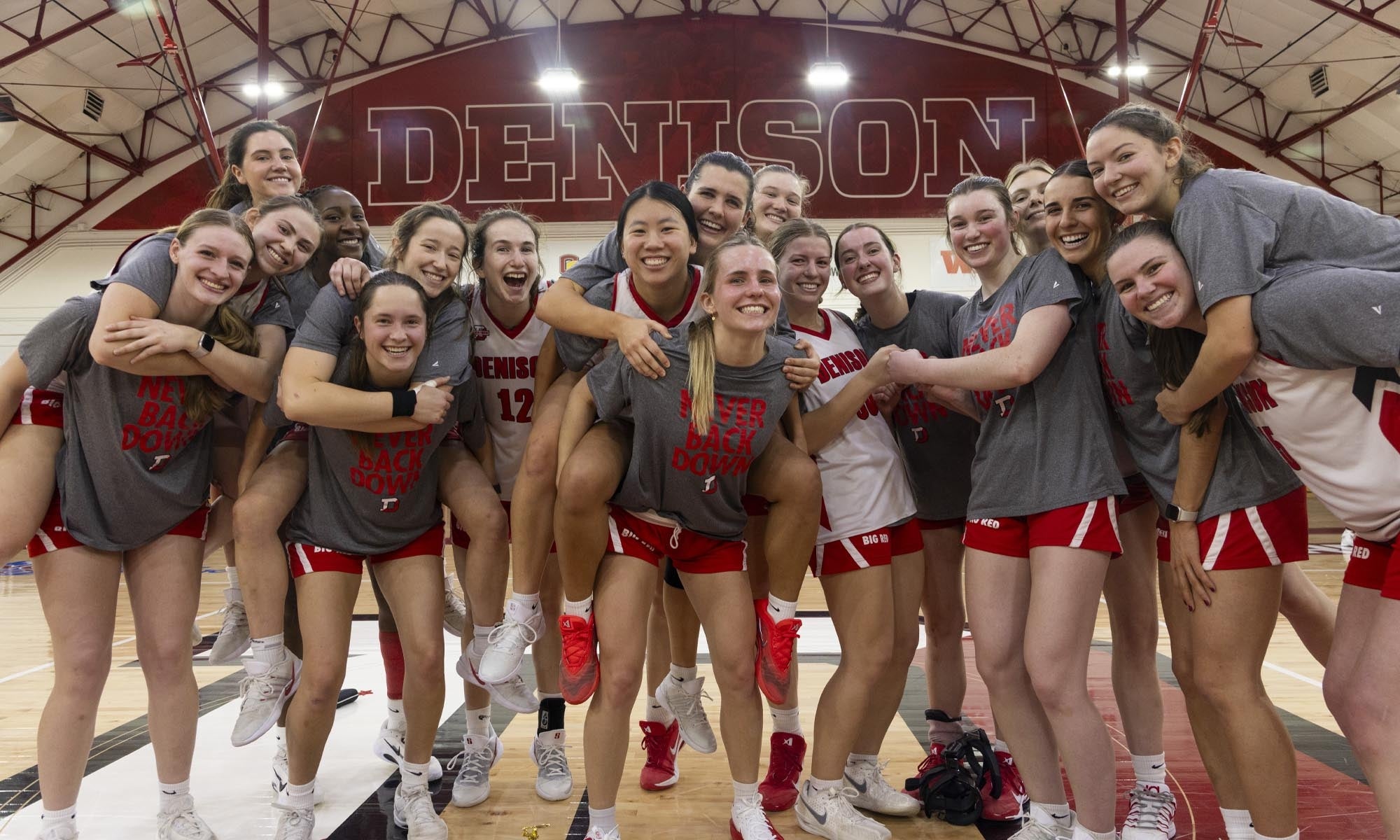 A team of collegiate women's basketball players in Denison tee shirts and shorts gathered on the court for a fun group photo.