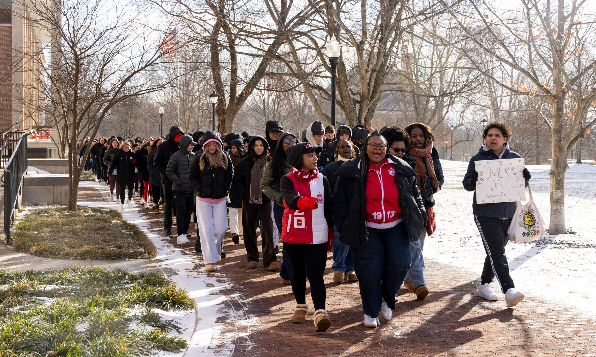 A group of people in winter coats walking in a march across a snow-covered campus.