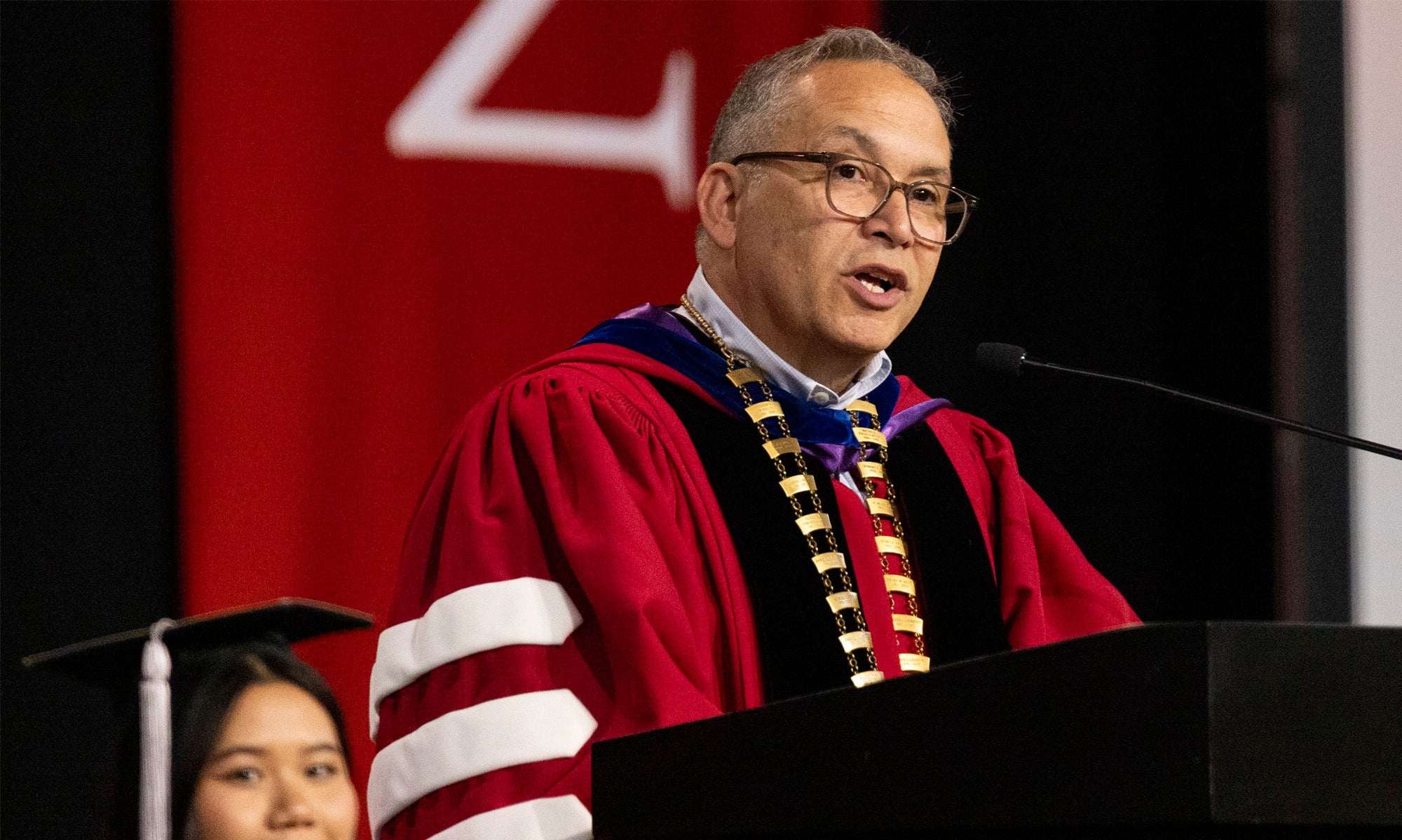 https://denison.eduAdam Weinberg in academic regalia speaks from a podium on a stage.