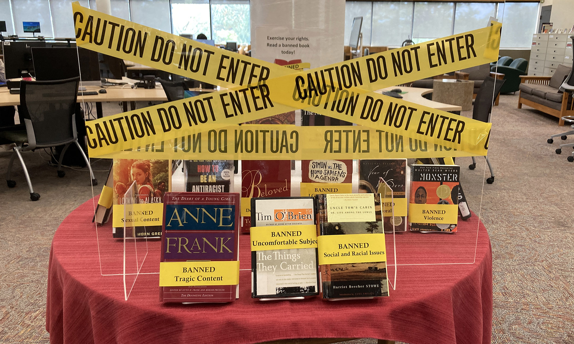 A display of banned books on a round table, wrapped in yellow CAUTION DO NOT ENTER tape.