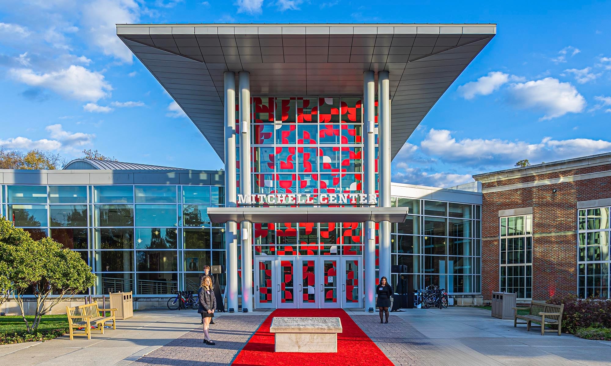 Front view of the Mitchell Recreation & Athletic Center main entrance with large glass windows, red accents, and a red carpet leading to the entrance under a modern overhang.