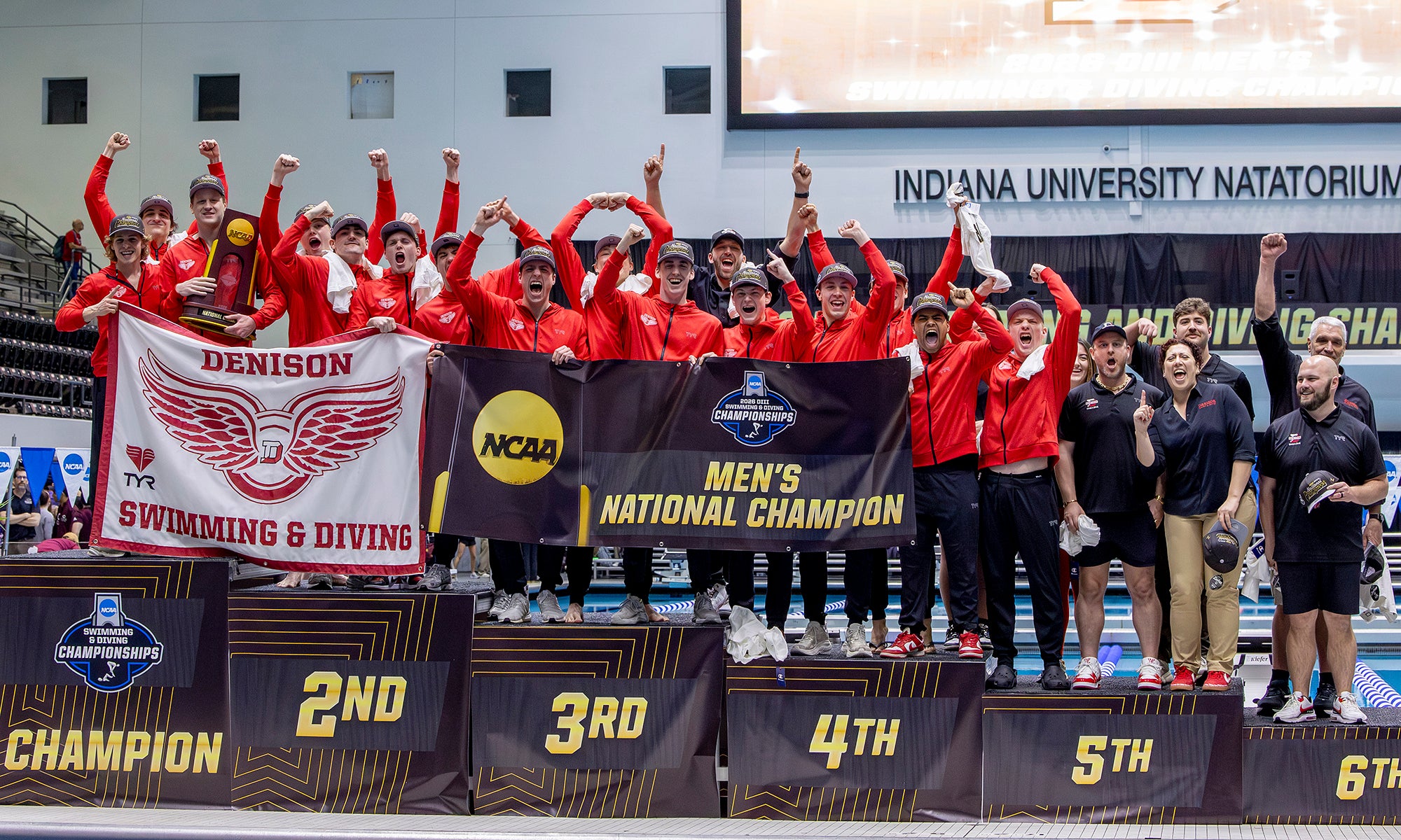The Denison swimming and diving team celebrates on the podium poolside after winning the national championship.