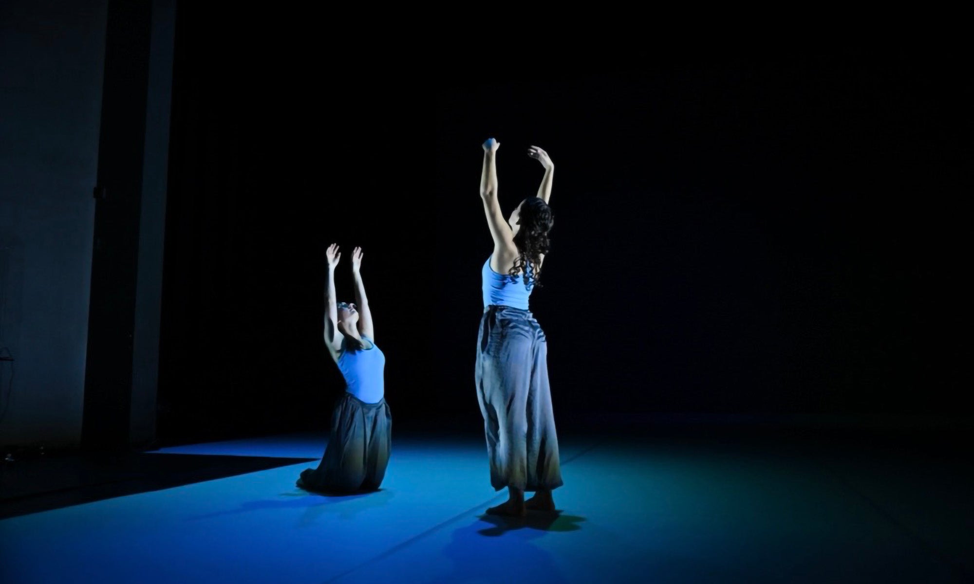 Two dancers in blue light performing on a stage.