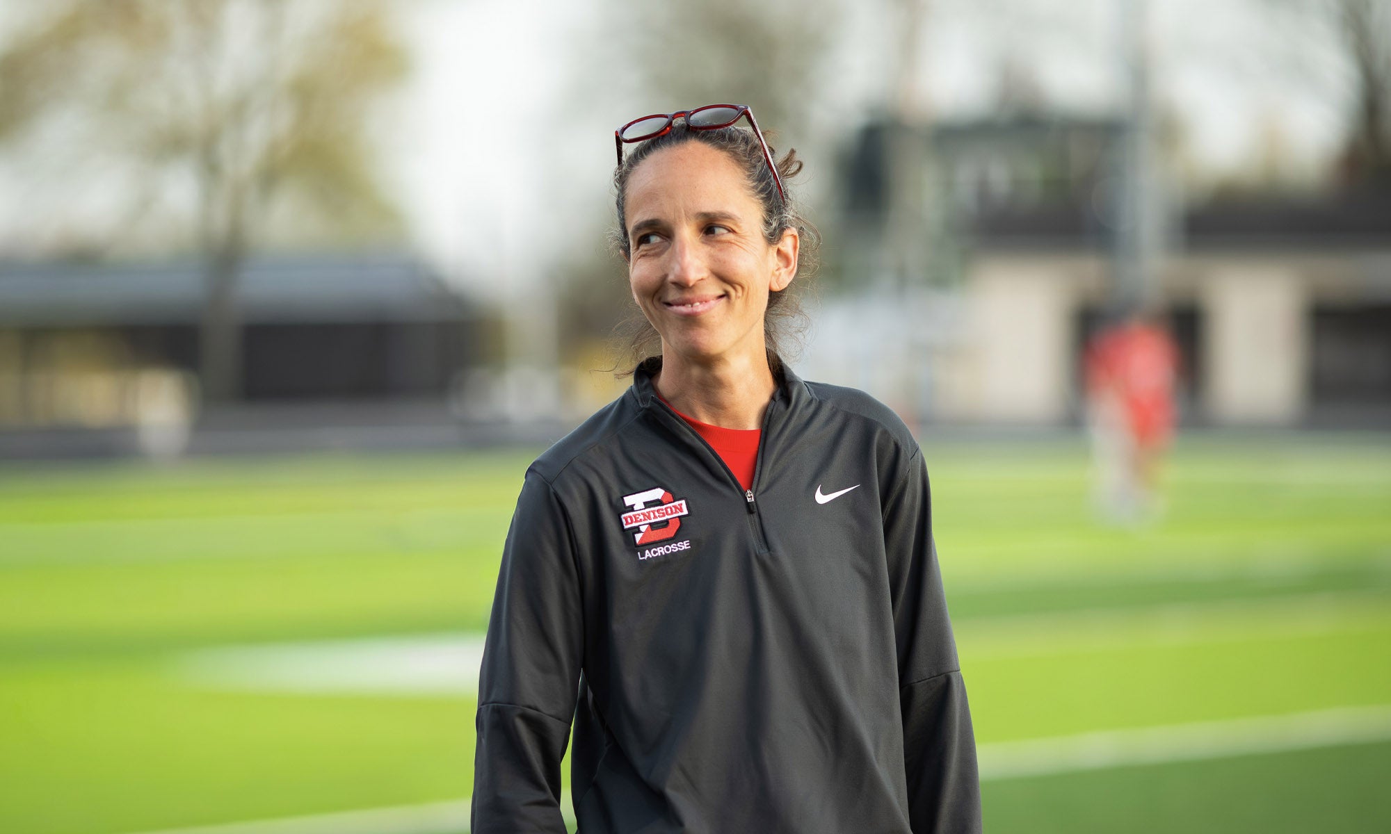 A woman with dark hair in athletic gear stands outside on a sports field.
