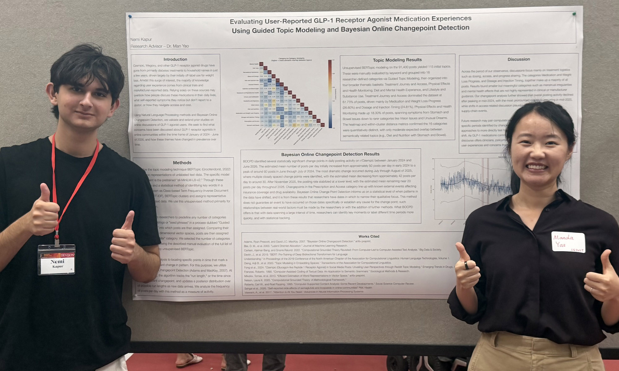 Two people stand in front of a scientific poster, both smiling and giving thumbs up, wearing name tags.