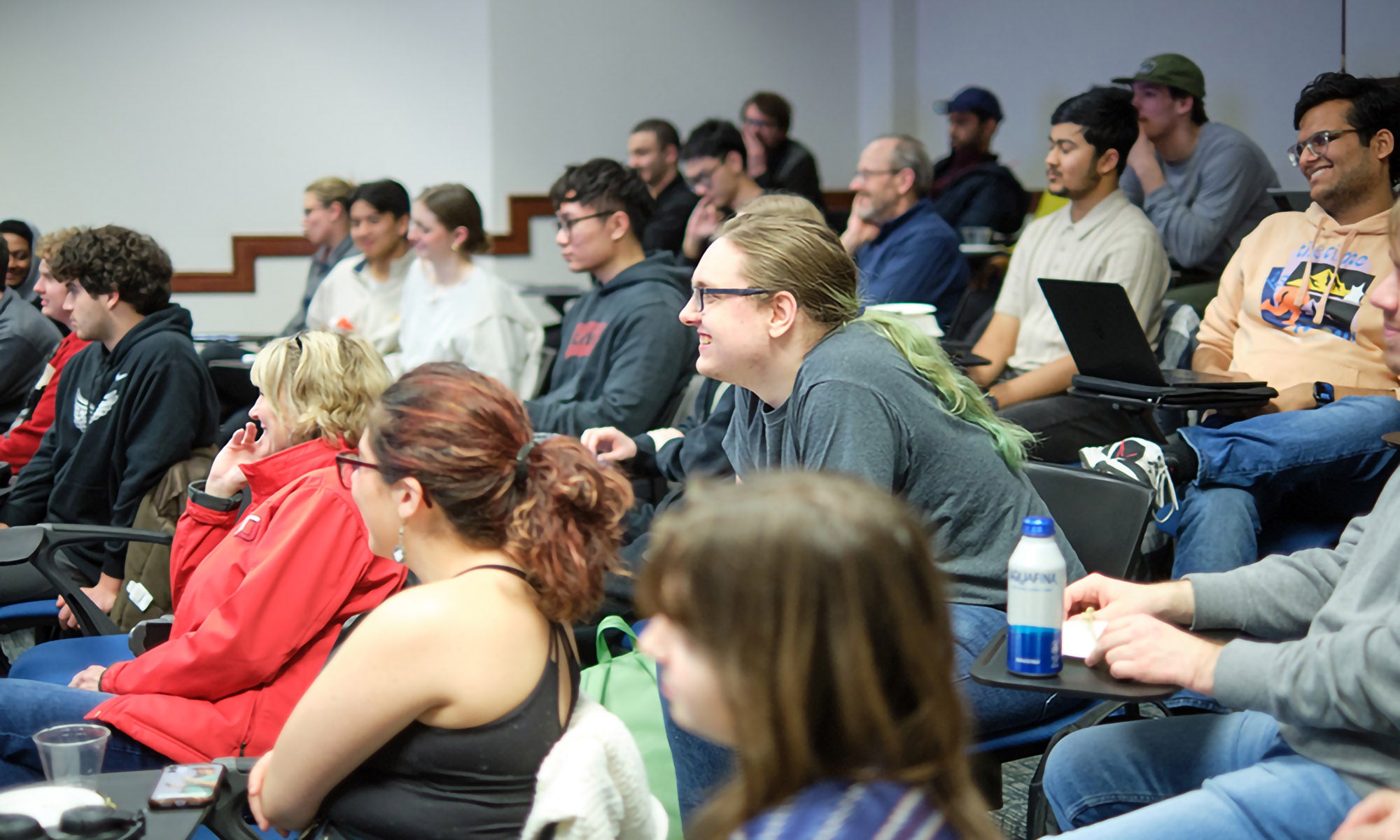 An auditorium-style lecture hall filled with students leaning in and actively listening to a lesson.