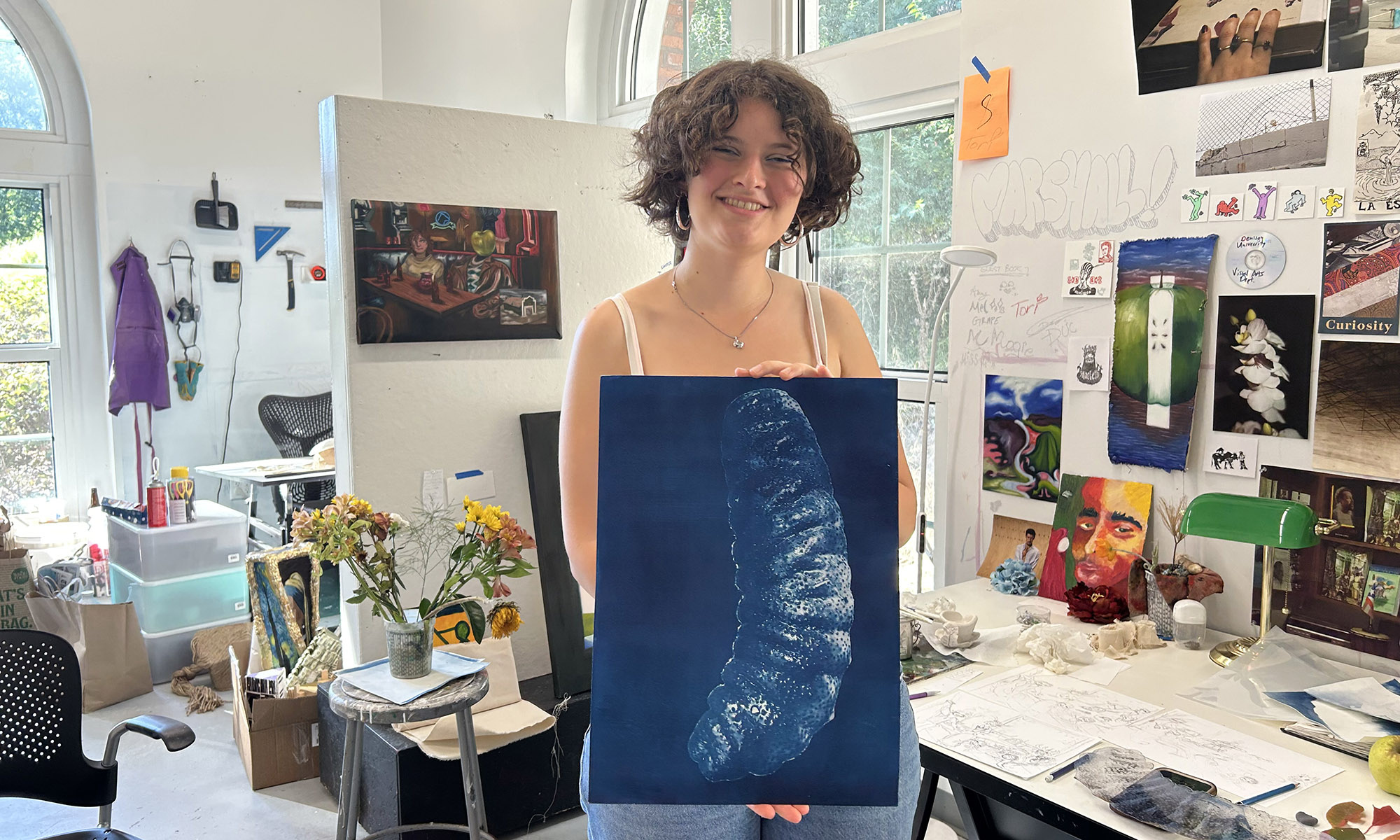 A smiling person in an art studio holding a cyanotype print.