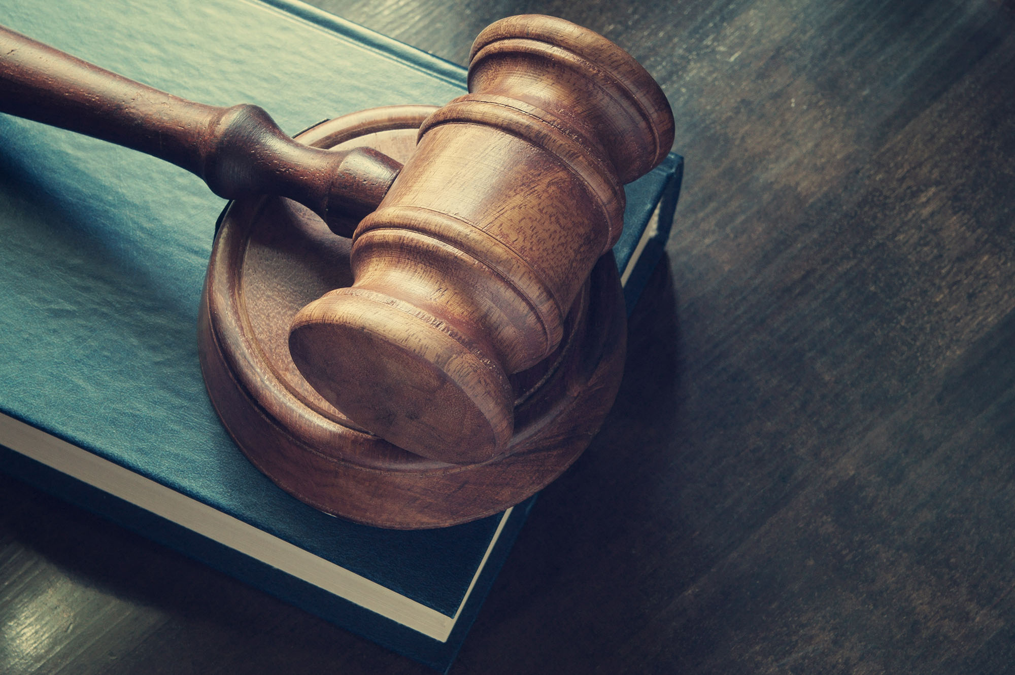 Image of a wooden gavel resting atop a green law book, both set on a dark brown wooden table.