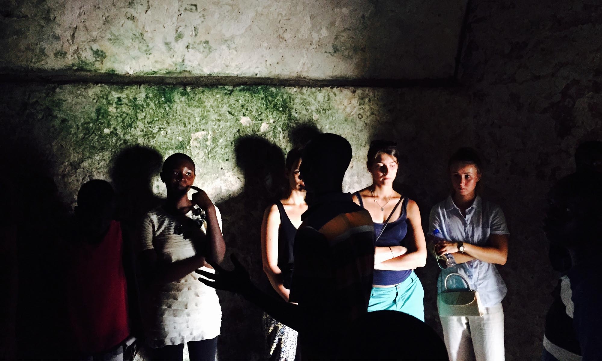 Students standing near a wall, illuminated by a bright light casting shadows behind them.