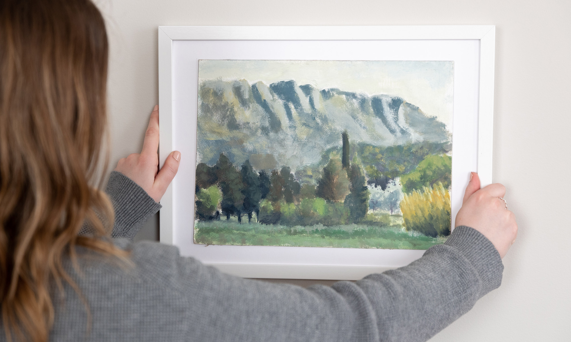 A woman hangs a painting on a gallery wall.