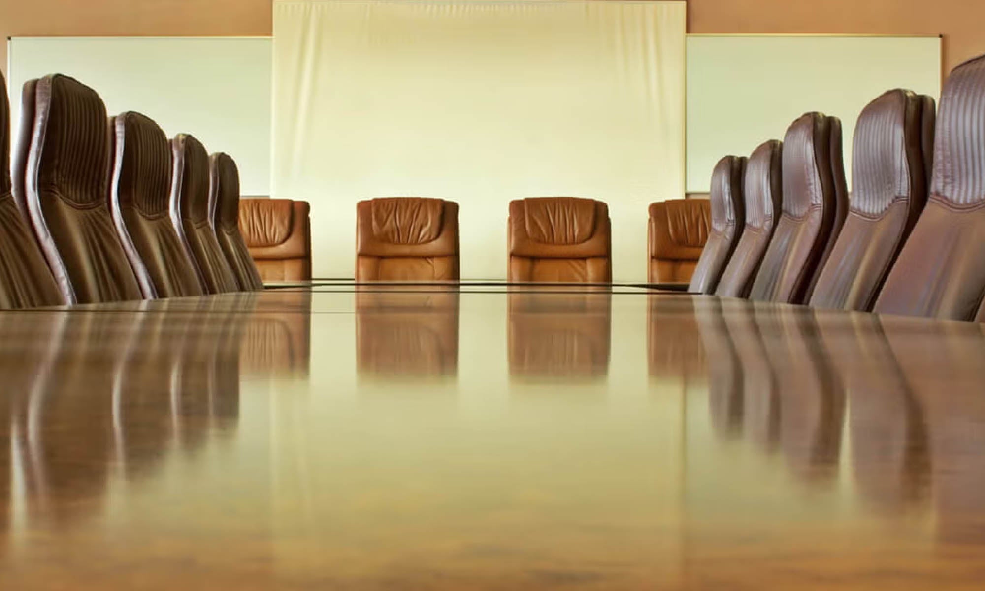 A boardroom table surrounded by tall leather chairs.
