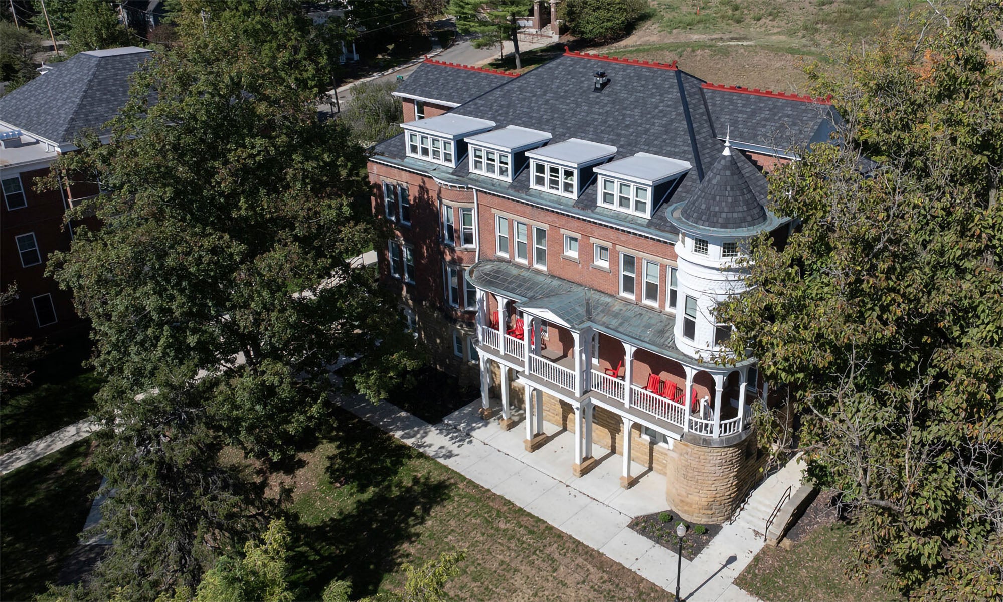 Aerial view of a three-story brick building with a turret, large porch, and white columns, surrounded by trees and a sidewalk.