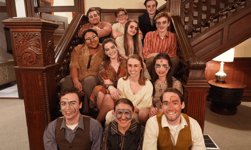The 12-person ensemble, wearing colorful makeup, sits on the inner staircase of the Mulberry House, where they are to perform their site-specific play.