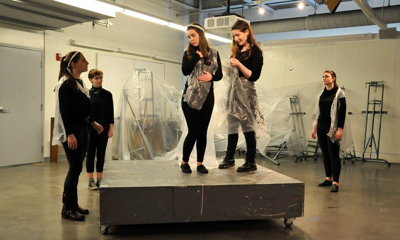 Five ensemble performers wearing black perform A Winter's Tale in the Bryant Arts Center. Two performers stand on a wheeled platform, draping themselves and the minimal set behind them in plastic sheets.