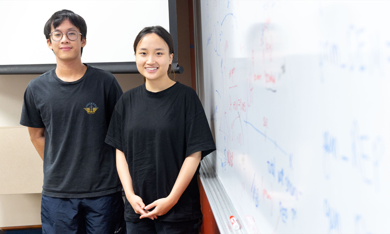 Photo of two Denison students Huy Phan and Linh Bui stand next to a dry-erase board filled with observations and notes.