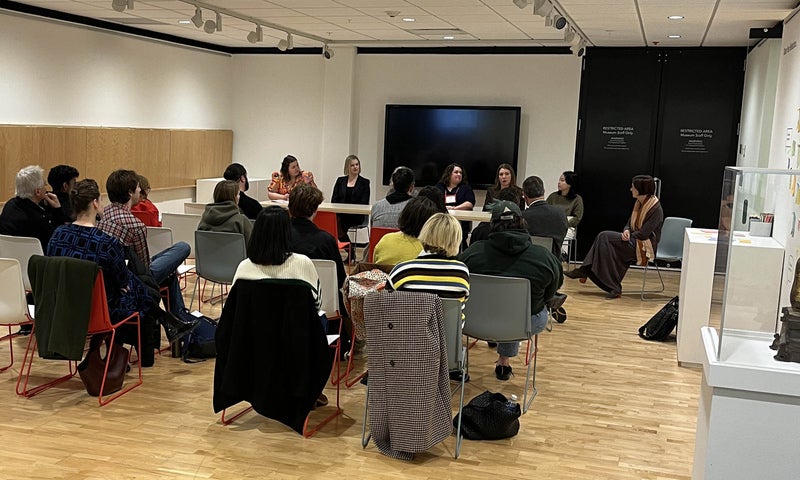 A group of people gathered in a museum gallery listening to a panel discussion. 