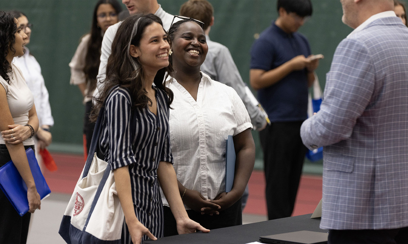 Two women meet with a company rep at a busy career fair.
