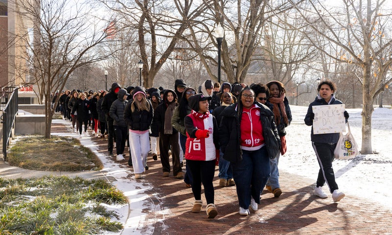 A group of people in winter coats walking in a march across a snow-covered campus.