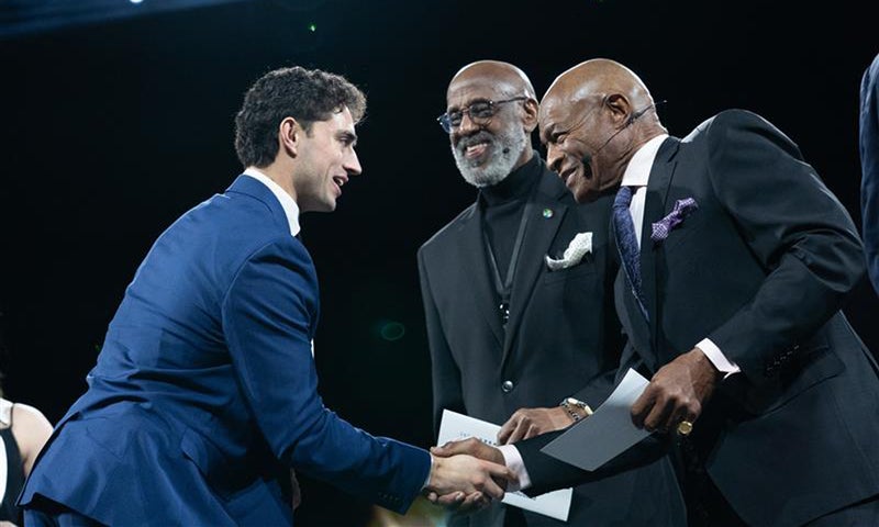 A man in a blue suit shakes hands with two men in suits as they hand him an award.