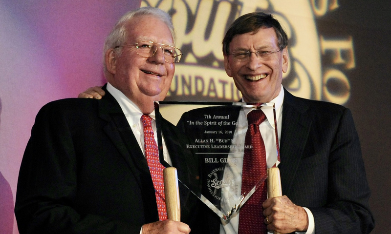 Two men in suits smiling and holding glass awards on a stage.