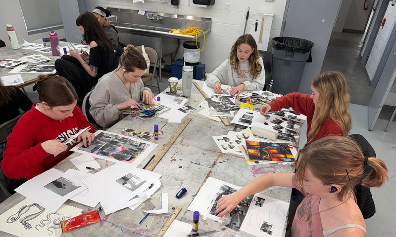 A group of people sit around a table filled with art supplies, creating art.