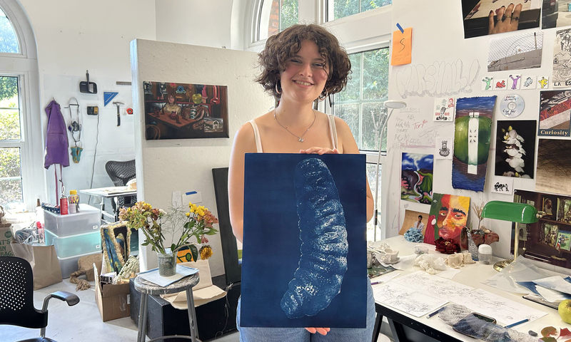 A smiling person in an art studio holding a cyanotype print.
