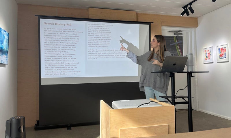 Zoe Ward ’28 stands in front of a projection screen displaying poetry text.
