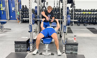 Denison student assists weightlifter with a rep on a weight bench in a gym.