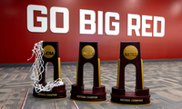 Three NCAA championship trophies lined up in front of a large red well with the white block letters that say "Go Big Red"