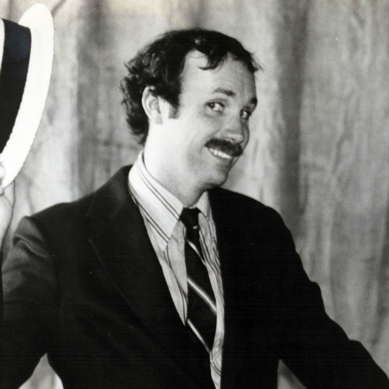 Photo of a young Gary McAvay in a suit and tie, holding a classic straw boater hat.